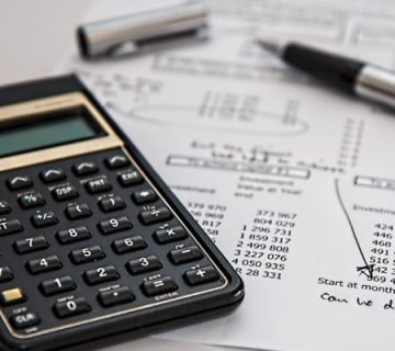 A financial desk setup featuring a TI-30Xa calculator, silver pen, and printed investment documents with handwritten notes and circled figures.
