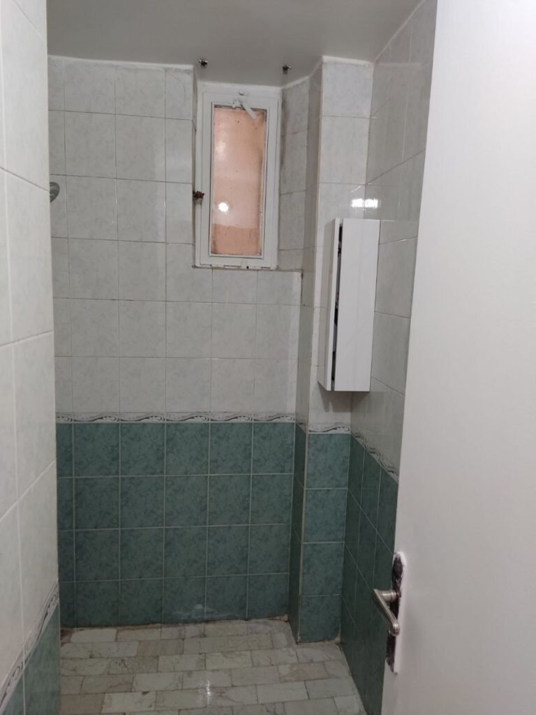 An outdated bathroom with old green and white tiles and traditional flooring before a complete modern renovation by Fardo Technical Services.